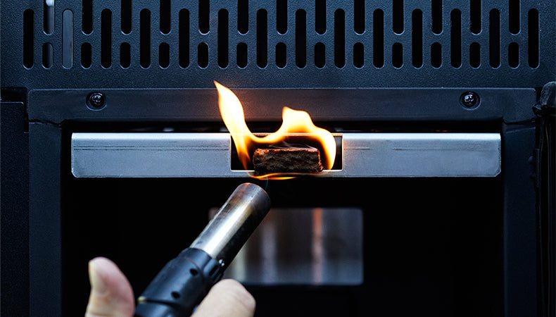 A person uses a lighter to set fire to a fire starter block inserted into a Gravity Series Grill & Smoker.