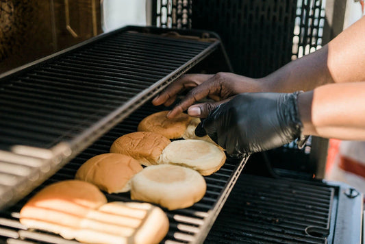 A person lays hamburgers buns on the warming rack of a Gravity Series grill