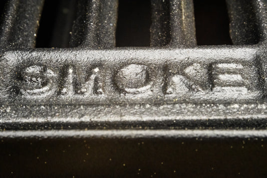 A grill grate with the word "SMOKE" embossed on the edge