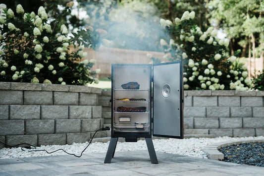 A vertical smoker open to show 3 racks of food sitting above the wood and water trays. The power cord with temperature control knob plugs into the bottom left side of the smoker.