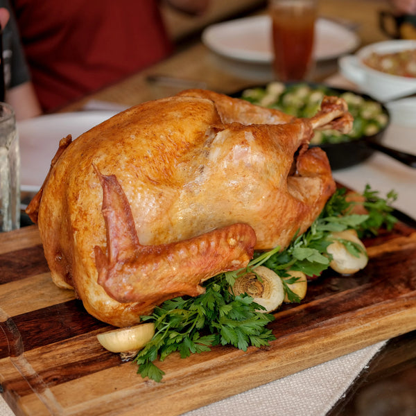 A fried turkey takes pride of place on a Thanksgiving table. The turkey is on a wooden board garnished with fresh parsley and cooked onions.
