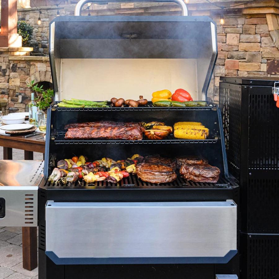 An open Gravity Series 1050 grill showing 3 racks of food including steaks, kabobs, ribs, and vegetables. Front shelf is folded down out of the way.