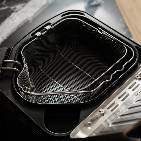 The basket sits inside on open, empty fryer. Two basket clips on the front of the basket rest in a slot in the fryer body to hold the basket out of any oil or water.