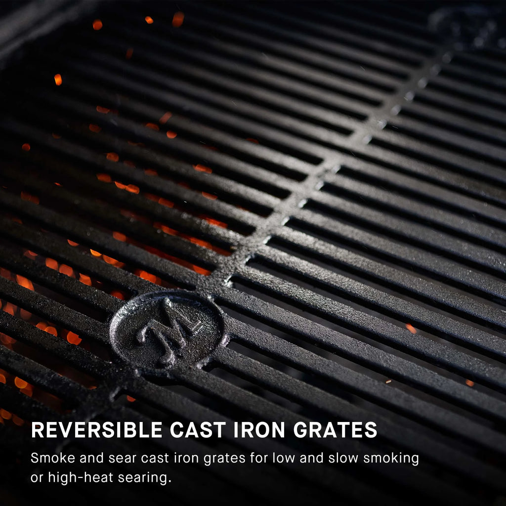 Reversible cast iron grates on a grill with visible Masterbuilt logo. Overlay text reads: Reversible cast iron grates. Smoke and sear cast iron grates for low and slow smoking or high-heat searing.