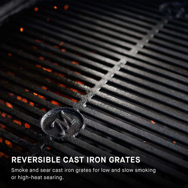 Reversible cast iron grates on a grill with visible Masterbuilt logo. Overlay text reads: Reversible cast iron grates. Smoke and sear cast iron grates for low and slow smoking or high-heat searing.