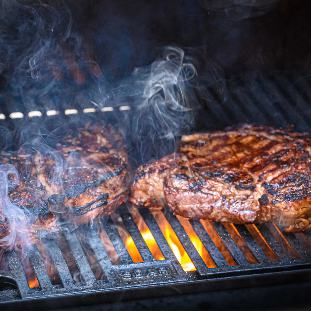 Steaks searing over flaming coals. The grill grate has a small section at the front with the word "Sear" embossed on it.