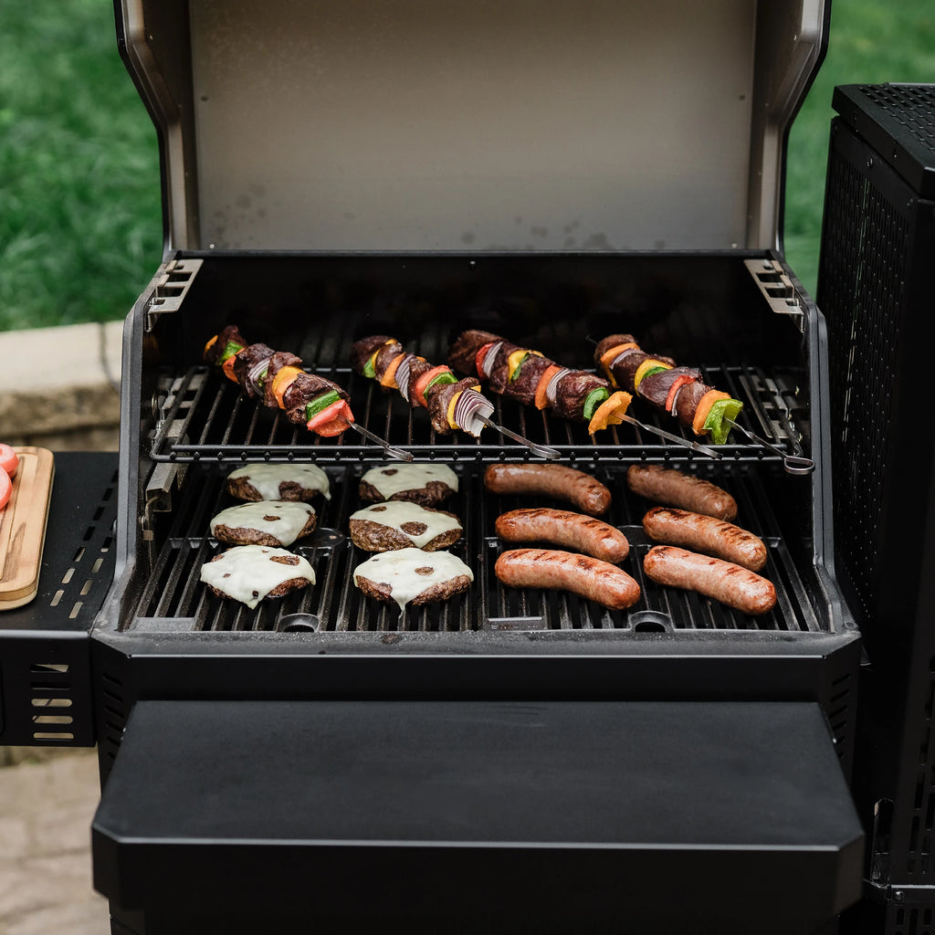 Open Gravity Series 600 grill with the front shelf up. Cheeseburgers, sausages, and skewers cook in the grill.