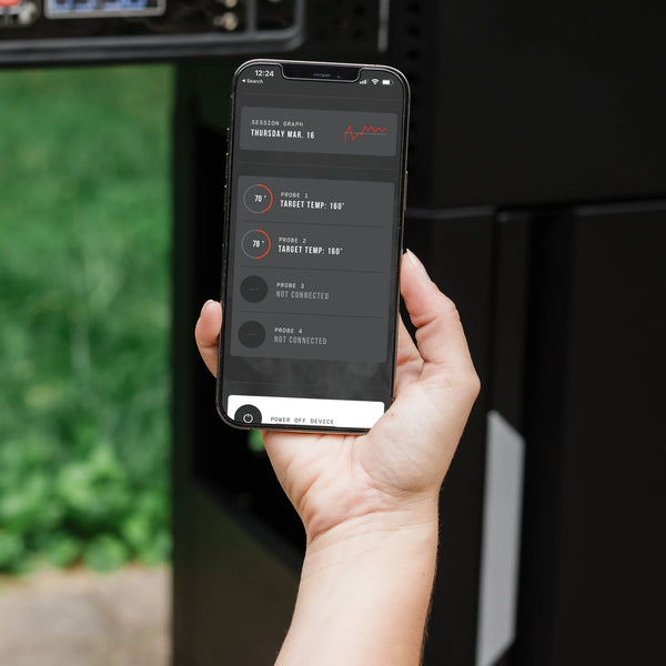 Someone holds a smartphone running the Masterbuilt App up in front of an AutoIgnite Grill and Smoker