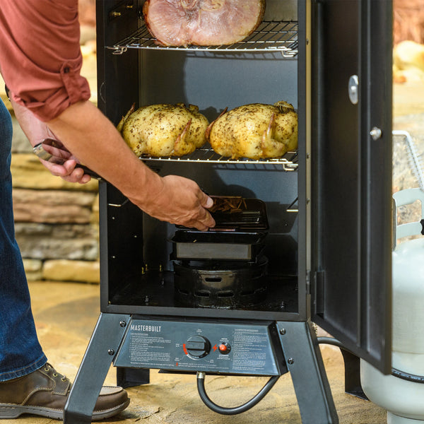 Person using a 30-inch, 2-rack Masterbuilt propane smoker with meats inside, outdoors.