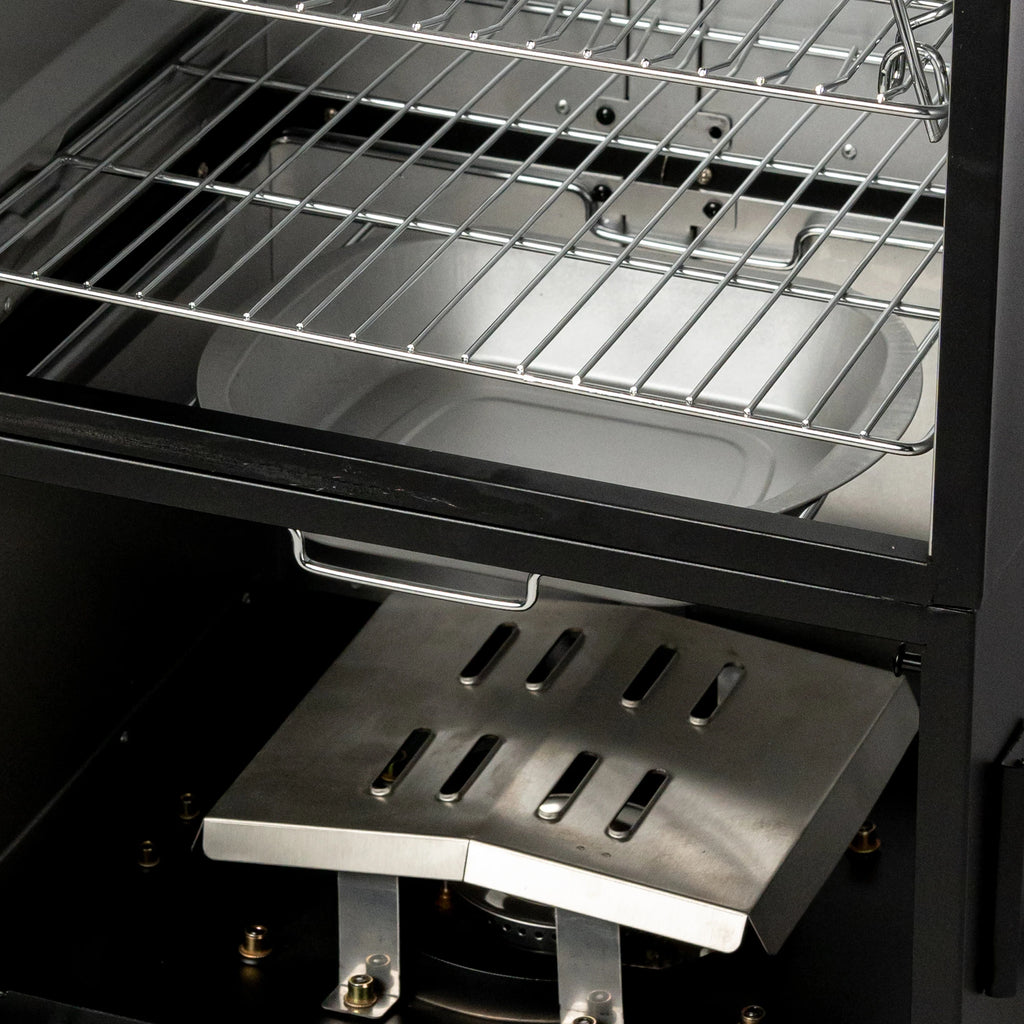 An empty water tray is visible above a slotted metal heat diffuser and burner box at the base of the smoker