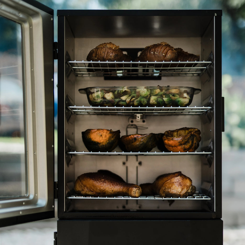 A variety of cooked meats and vegetables sit on the four racks of an open smoker