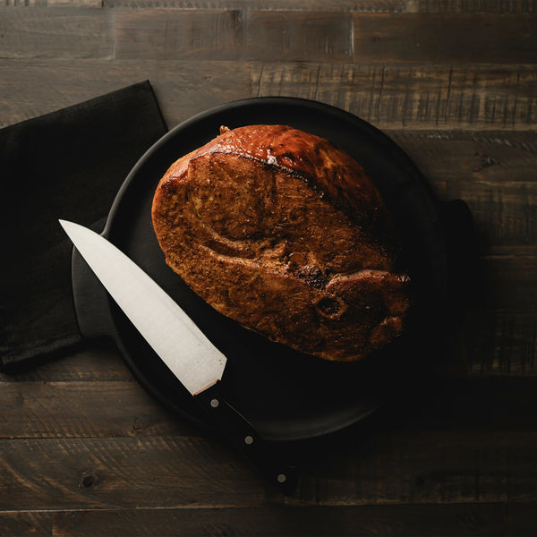 Smoked ham on a black plate with a knife on a wooden surface