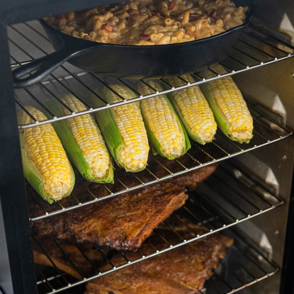 4 racks of food cooking in the smoker including ribs, corn on the cob, and macaroni and cheese.