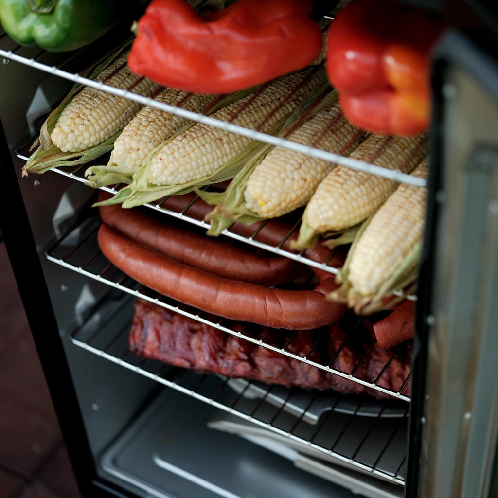 Four racks of food in the smoker including, top down, whole bell peppers, corn on the cob, sausage, and ribs.