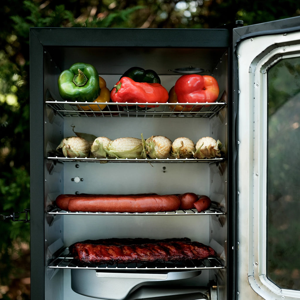 A Masterbuilt electric smoker with its door open, showing shelves with peppers, corn, sausage, ribs, and a removable water tray inside.