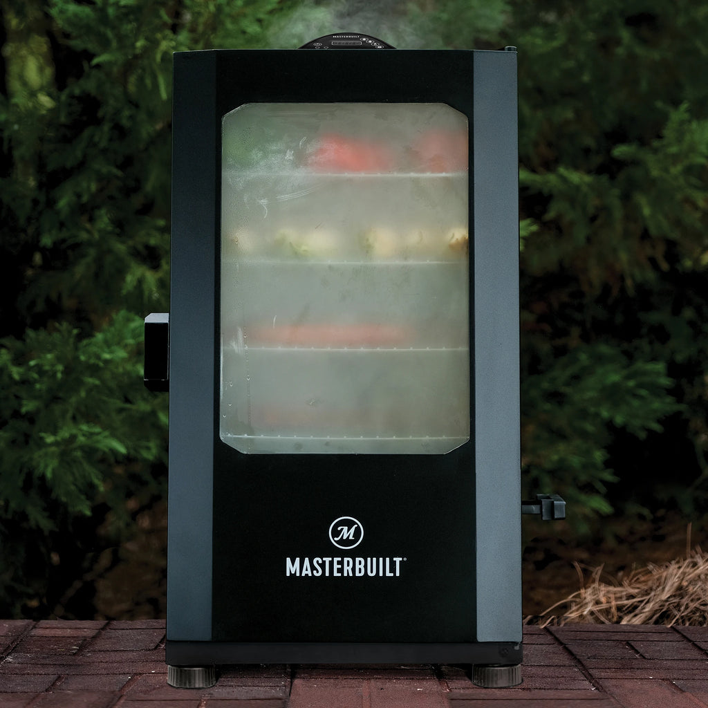 Masterbuilt smoker with food inside on a brick deck with greenery in the background