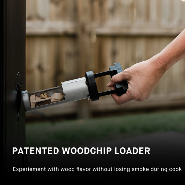 Patented woodchip loader: experiment with wood flavor without losing smoke during cook. A man uses the side woodchip loader to add wood chips to the smoker. The loader is a horizontal metal cylinder with an opening to add the chips. The cylinder has a black plastic handle used to push, pull, and turn the loader. 