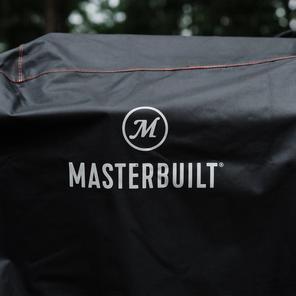 The Masterbuilt name and logo printed in white on the black grill cover. Several of the seams, double-stitched with orange thread, are visible.