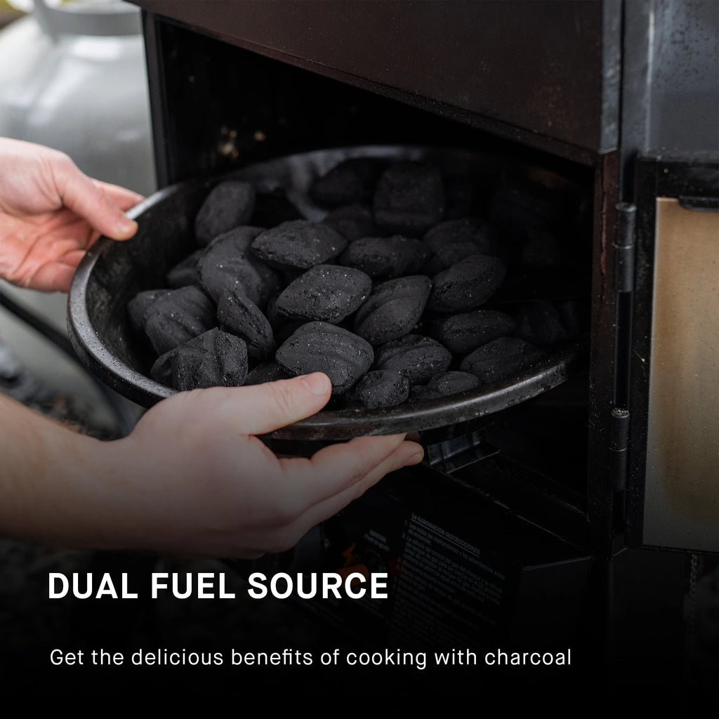 A person places the flame disk bowl full of charcoal briquettes into the bottom section of the smoker body. Text reads: Dual fuel source. Get the delicious benefits of cooking with charcoal. 