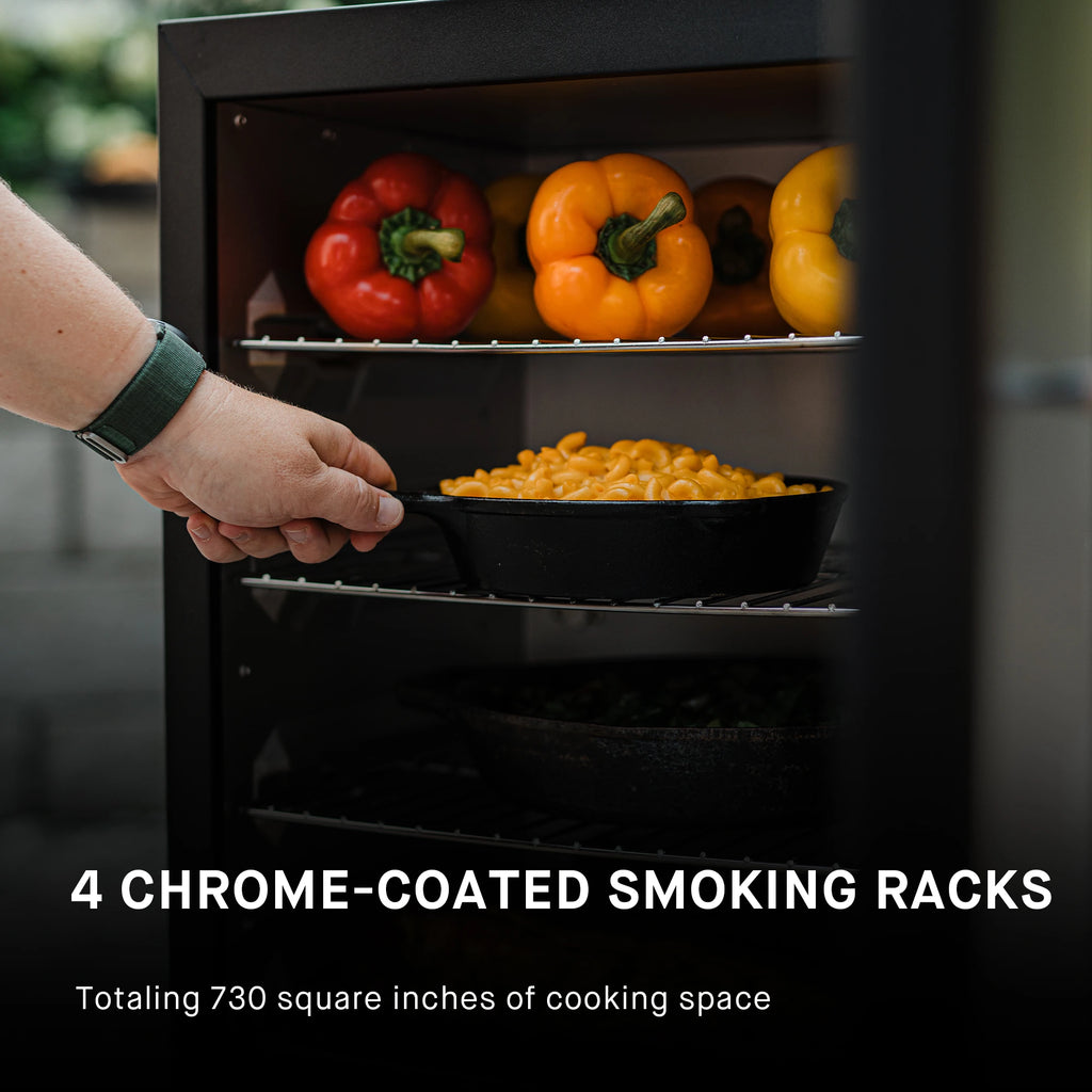 Person placing a pan of food into a smoker with whole peppers on the rack above. Text reads: 4 chrome-coated smoking racks totaling 730 square inches of cooking space.