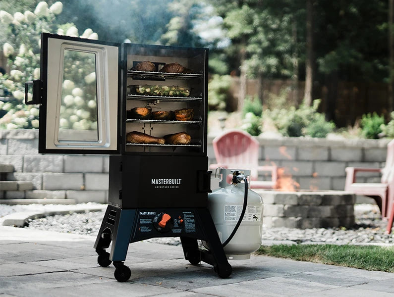A ThermoTemp smoker with propane tank attached sits on a patio. The smoker door is open to show 4 racks of food. The smoker is on legs with wheels. The orange temperature control dial and auto-ignite switch are on a control board between the smoker legs.
