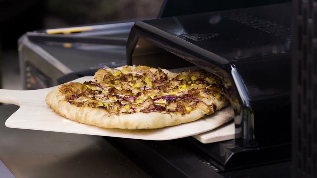 Using a wooden pizza peel to remove a cooked pizza being removed from a Masterbuilt Pizza Overn